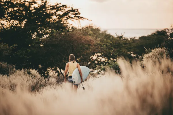 Surfer walking through bush toward ocean